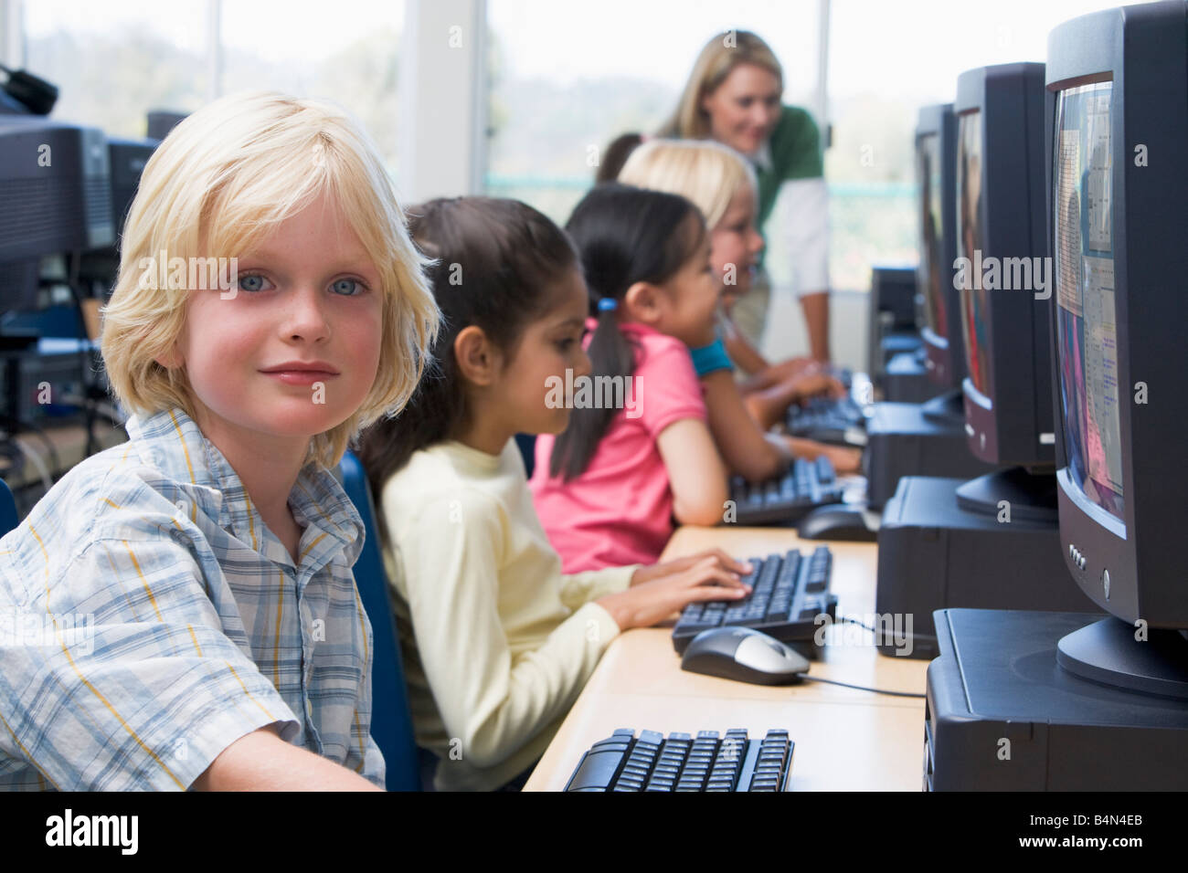 Les enfants devant un ordinateur avec l'enseignant en arrière-plan (profondeur de champ/high key) Banque D'Images