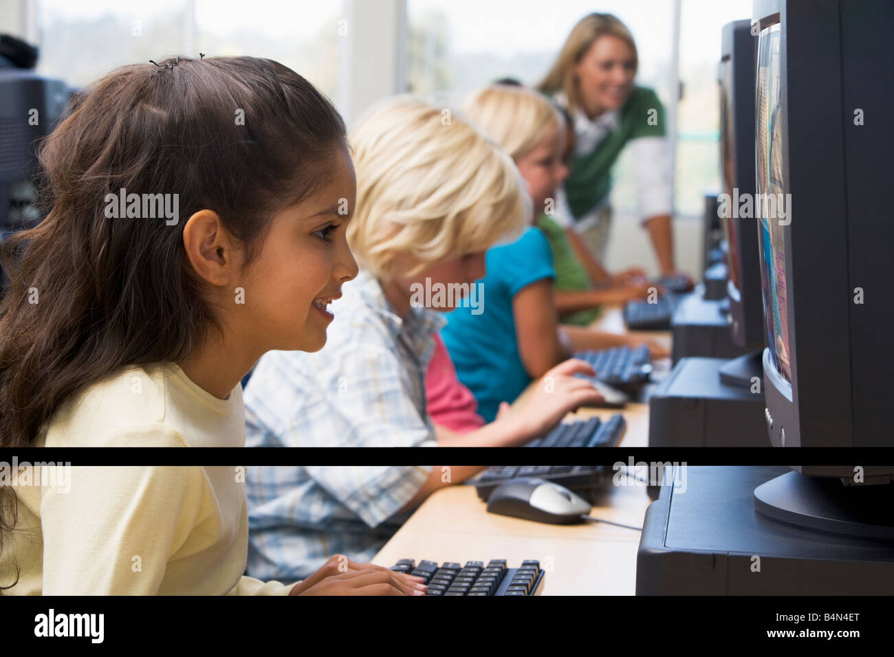 Les enfants devant un ordinateur avec l'enseignant en arrière-plan (profondeur de champ/high key) Banque D'Images