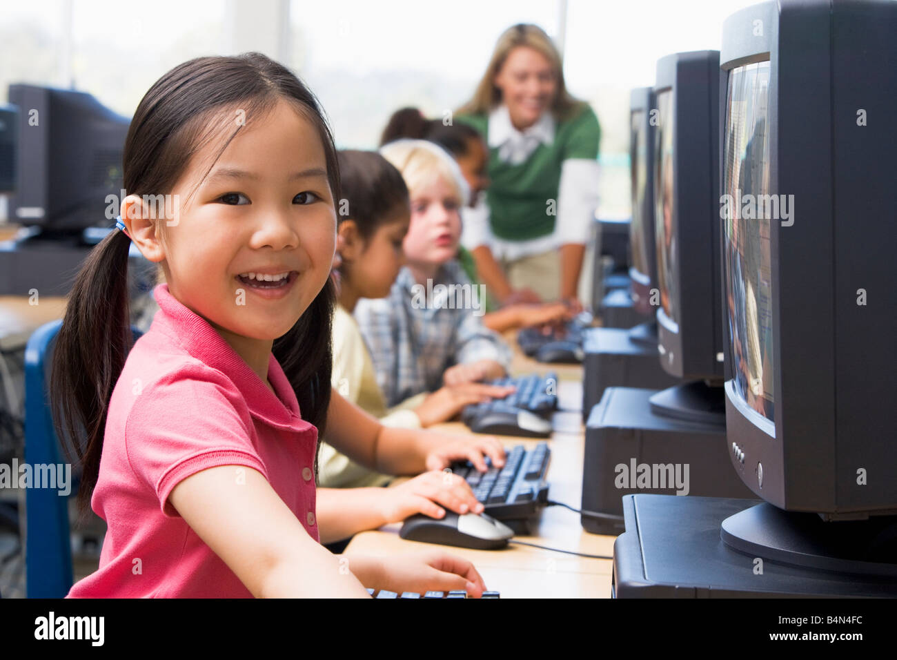 Les enfants devant un ordinateur avec l'enseignant en arrière-plan (profondeur de champ/high key) Banque D'Images