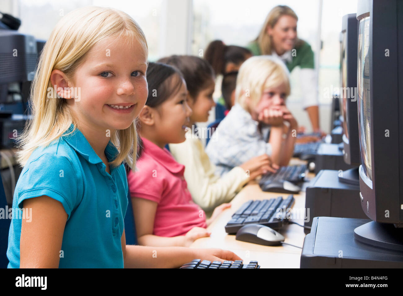 Les enfants devant un ordinateur avec l'enseignant en arrière-plan (profondeur de champ/high key) Banque D'Images