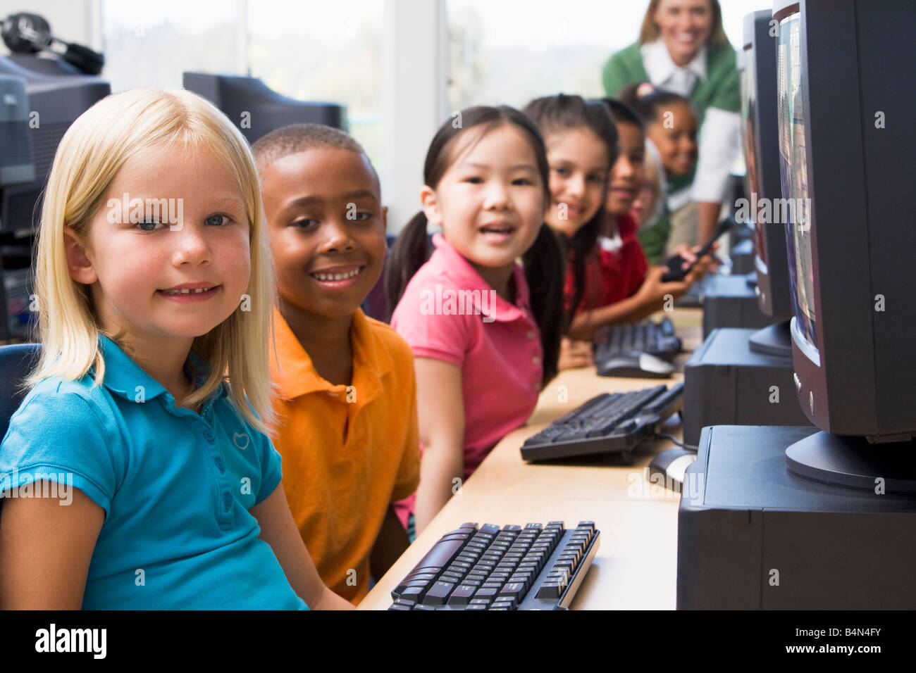 Les enfants devant un ordinateur avec l'enseignant en arrière-plan (profondeur de champ/high key) Banque D'Images