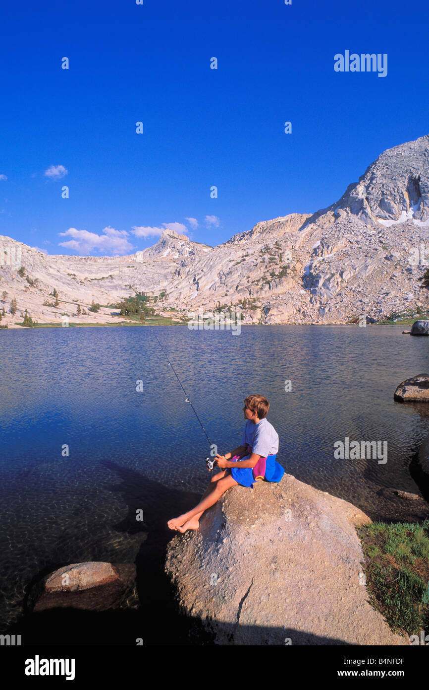 Garçon de pêche à partir d'un rocher sur le rivage de Tuolumne Meadows area Budd Lake Yosemite National Park California Banque D'Images