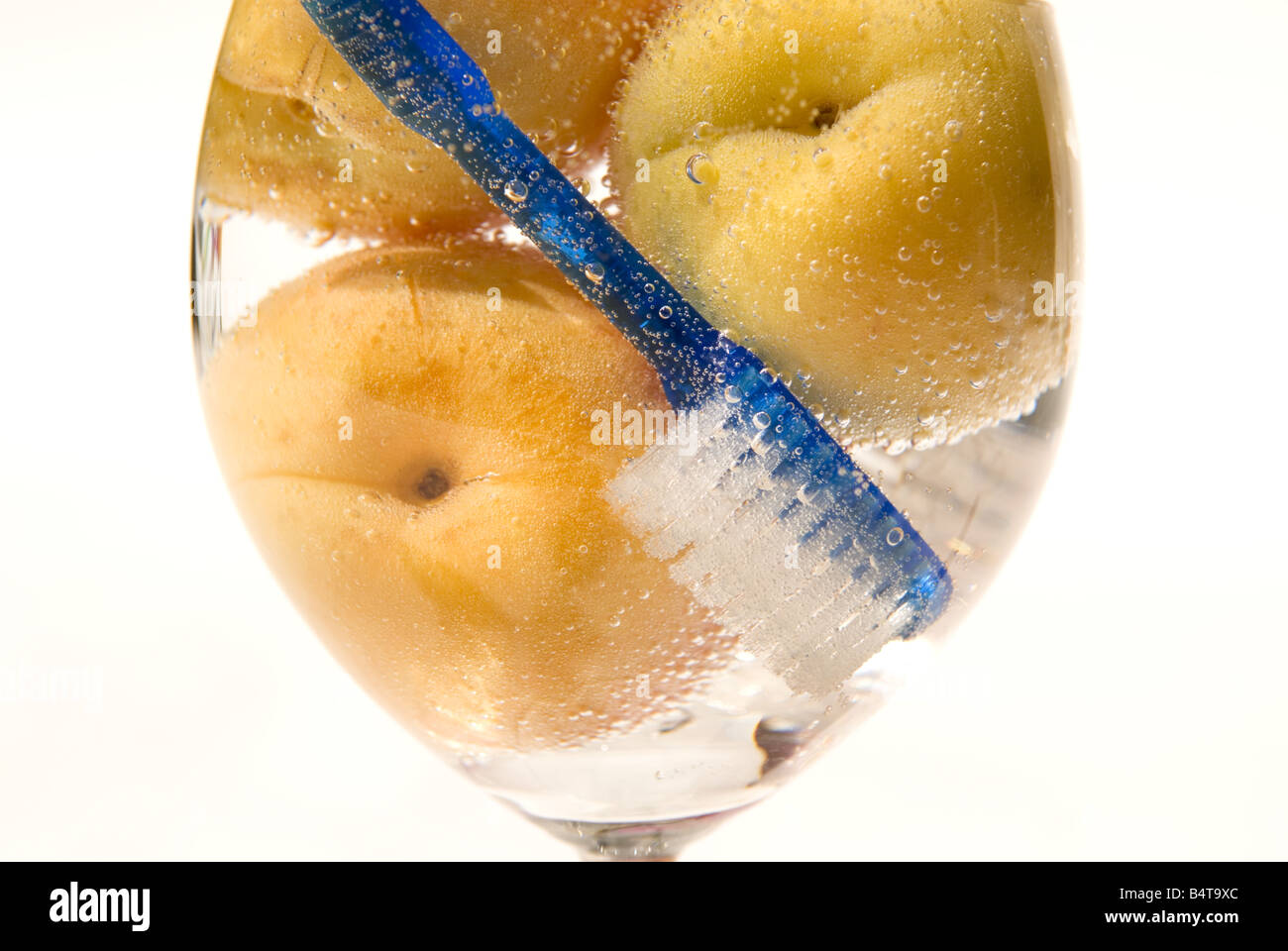 Close up d'abricots et brosse à dents bleu immergé dans un verre à vin rempli de fizzy eau claire Banque D'Images