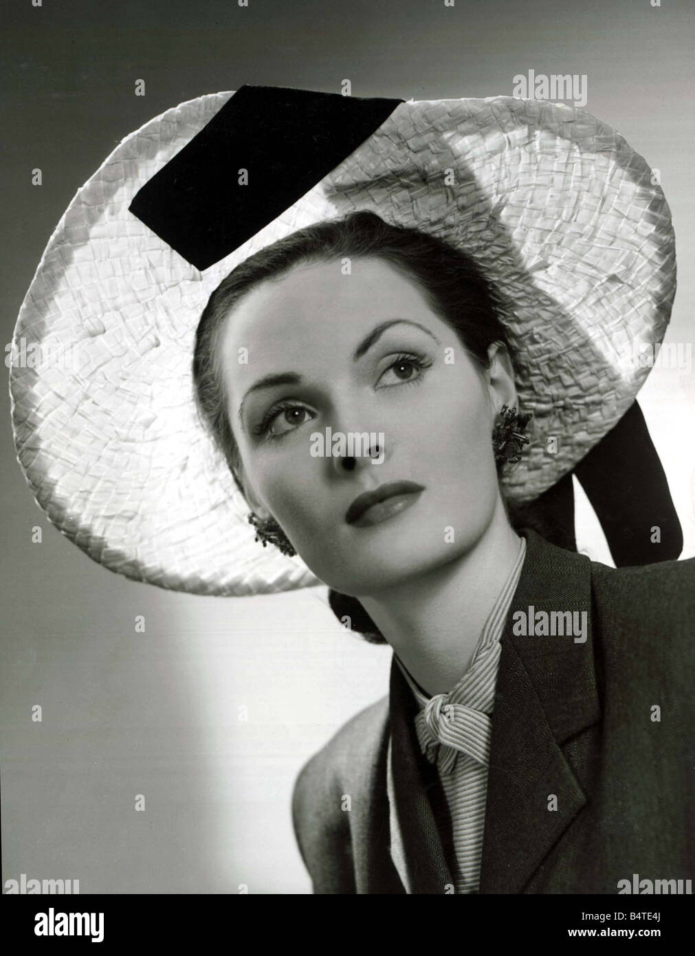 Vers 1940 La mode paille tressée naturel photo hat conçu par Hugh Beresford avec ruban de velours noir enfilées par le bord et de tomber sur l'épaule de grandes boucles d'une Cravate et veste blazer sur un modèle 1940 vêtements mode shoot mirrorpix Banque D'Images
