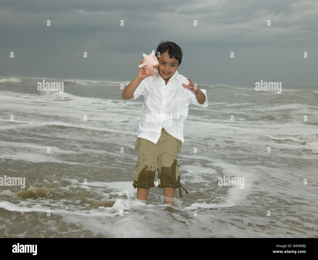 Asian boy écouter une conque à la plage Banque D'Images