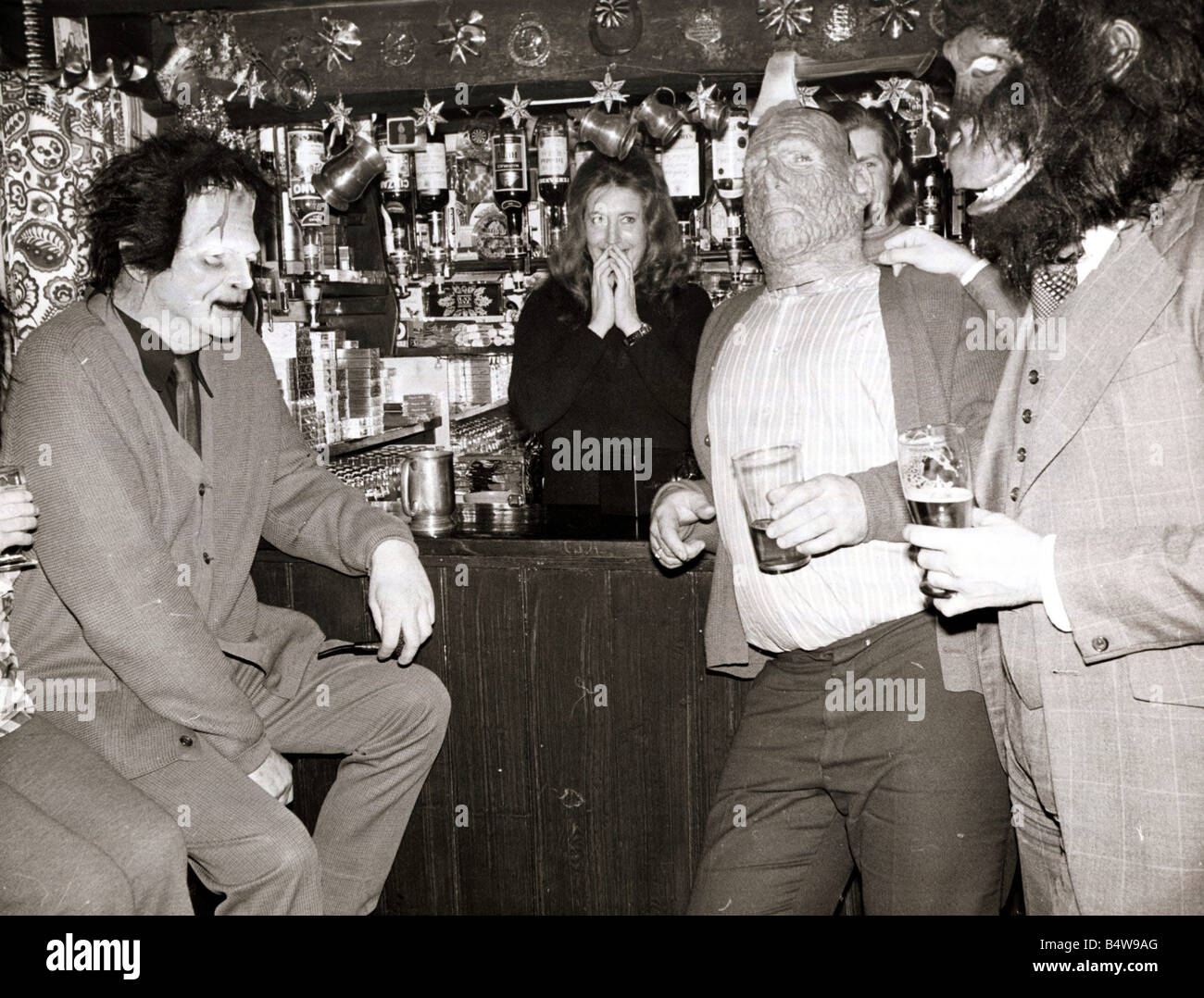Barmaid est confronté à un homme habillé comme Frankensteins Monster un autre homme avec une éclos enfouis dans sa tête et un couple de gorilles au cours d'une robe de soirée au Red Lion Pub à Kings Langley Hertforshire Janvier 1975 Banque D'Images
