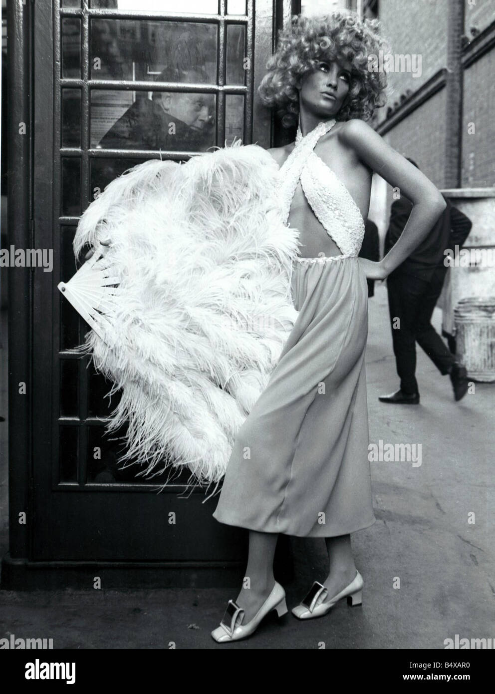 Fashion 1960 Model wearing style années 30 en mousseline Beige culottes maxi avec un sequin corsage blanc mini non officiel d'une plume ventilateur avec un afro hair style téléphone rouge fort Banque D'Images