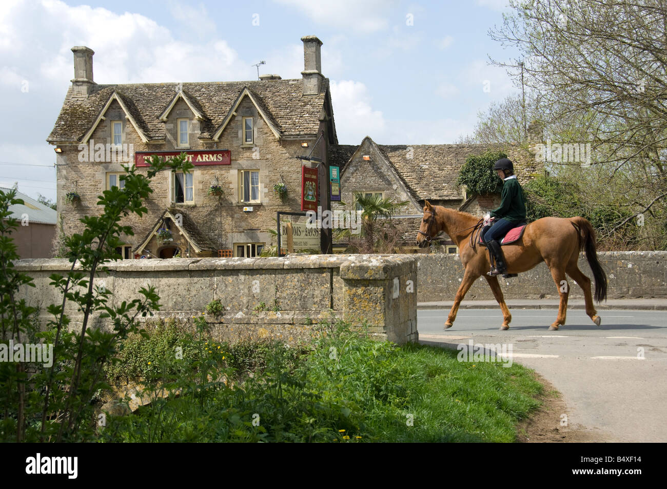 Cheval et cavalier traversant un pont de pierre sur la rivière Colne dans le village de Cotswold SOUTH CERNEY, CIRENCESTER, Gloucestershir Banque D'Images