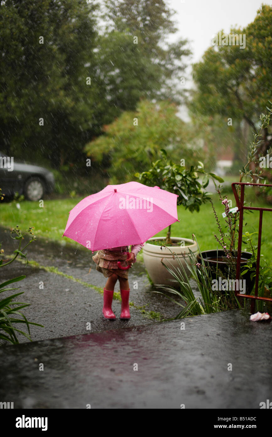 Fille dans la pluie avec un parapluie rose vieux de cinq ans Banque D'Images