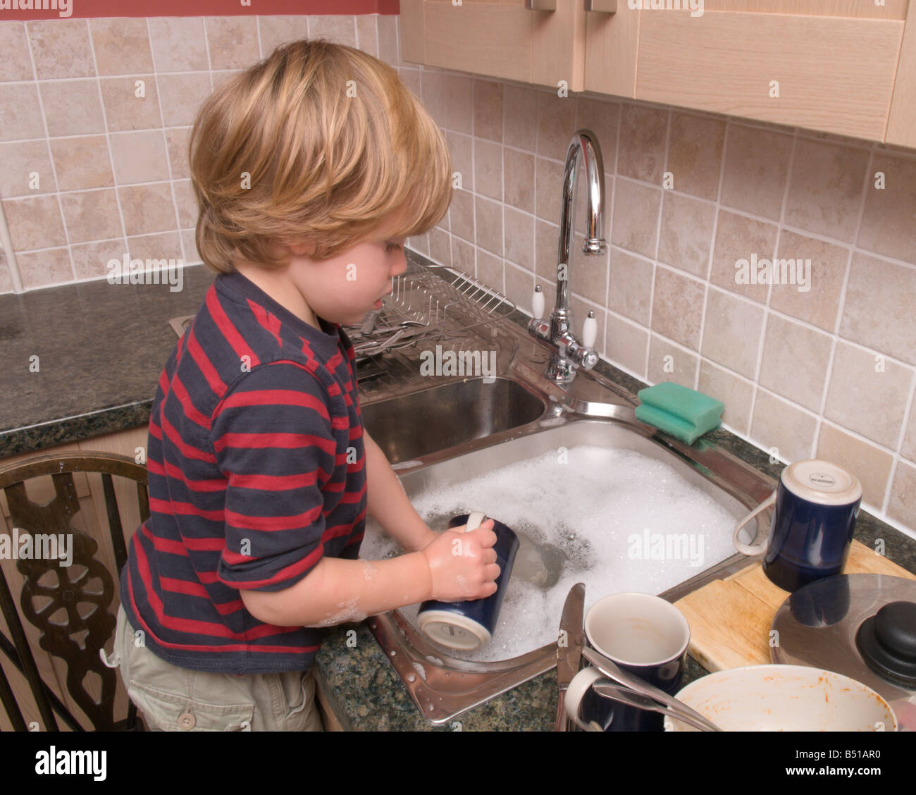 Bébé garçon enfant de l'évier de la cuisine en faisant la vaisselle avec  eau chaude robinet ouvert Photo Stock - Alamy