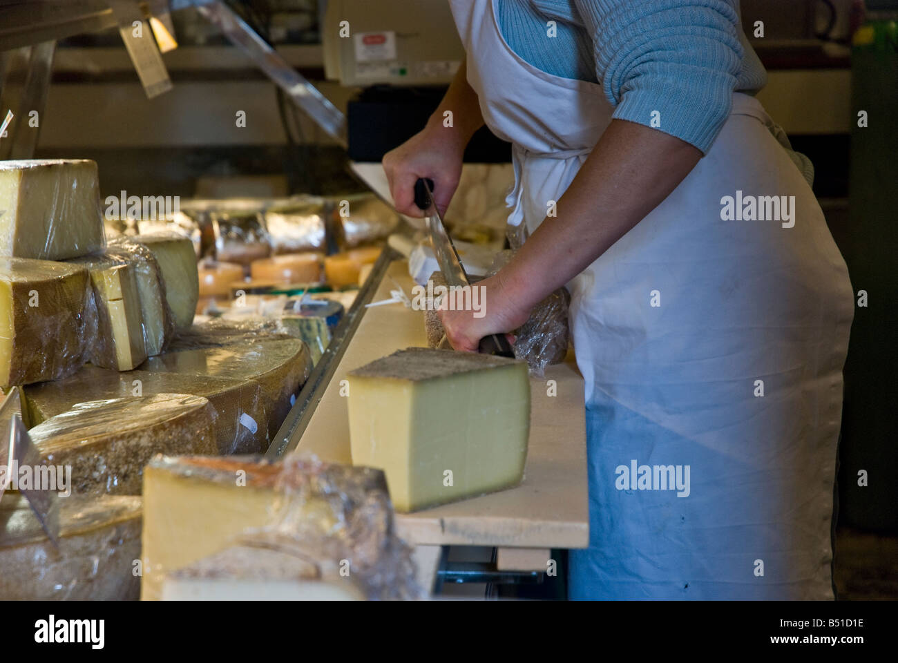 Femme fromager en découpant une tranche de gruyère pour un client Banque D'Images