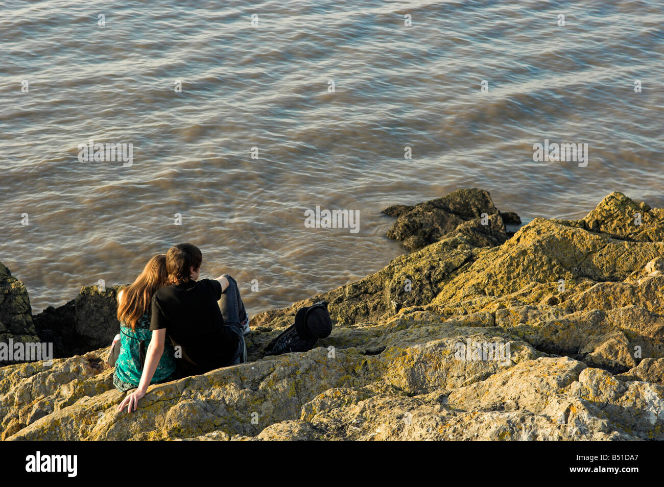 Jeune couple assis sur des rochers surplombant la mer Banque D'Images