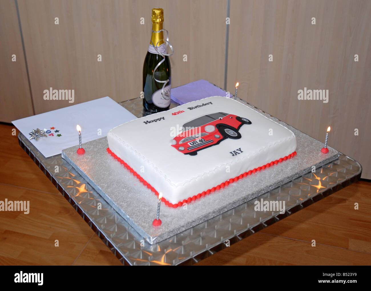 Square 40e anniversaire gâteau décoré avec l'image du mini-Cooper, avec quatre cartes et allumé des bougies et du champagne Banque D'Images