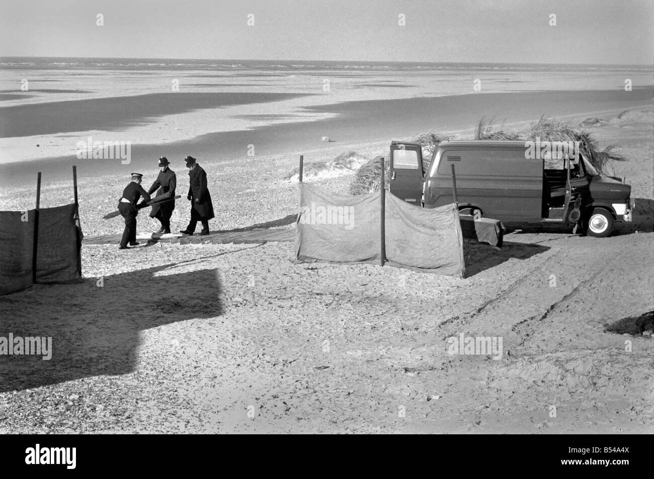 Femme morte trouvée sur la plage au fleuve Annexe. Scène de la tragédie montrant brûlé reste de ce qui semble être un matelas, un cercueil derrière des écrans, et un fourgon de police sur les lieux, gardé par des policiers. ;Novembre 1969 ;Z10766-002 Banque D'Images