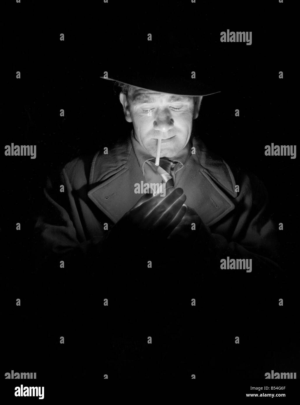 Un détective privé allume une cigarettte dans une ruelle sombre chemin tout en transportant ses enquêtes;personnes dispose d;cigarette éclairage;comparaison blindés par mains;fumeurs  ; Trilby hat coat Vêtements;Décembre 1953 ; Mirrorpix Banque D'Images