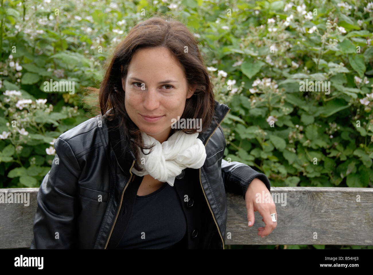 Jeune femme brune assise sur un banc, écharpe blanche, veste en cuir, England, UK Banque D'Images