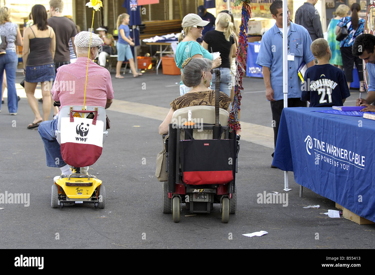 Un couple de personnes âgées bénéficie d'un voyage à un événement public à leur mobilité scooter et fauteuil roulant motorisé. Banque D'Images