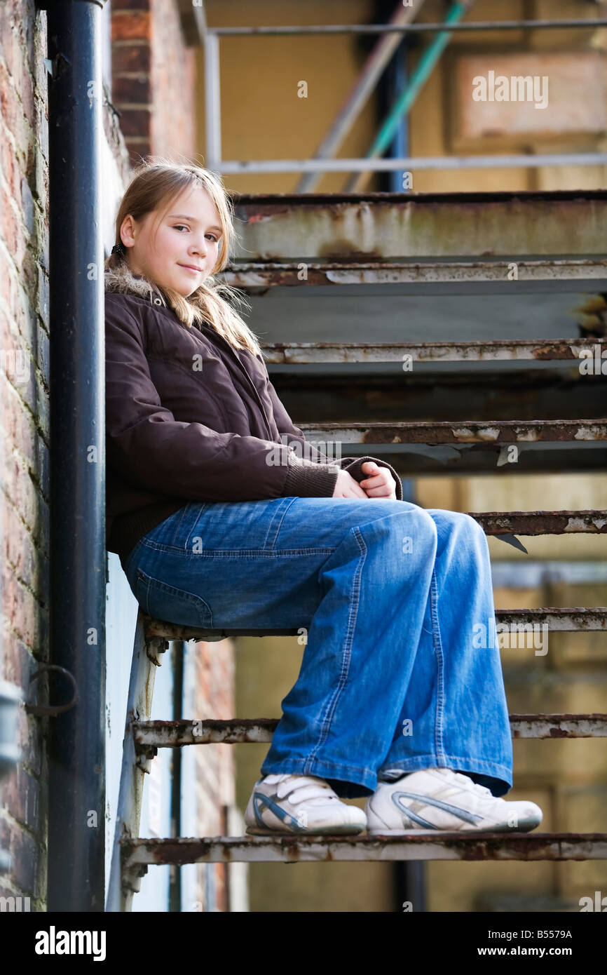 Teenage girl (11-13 ans) assis sur un certain nombre de mesures à l'extérieur d'un bâtiment ancien Banque D'Images