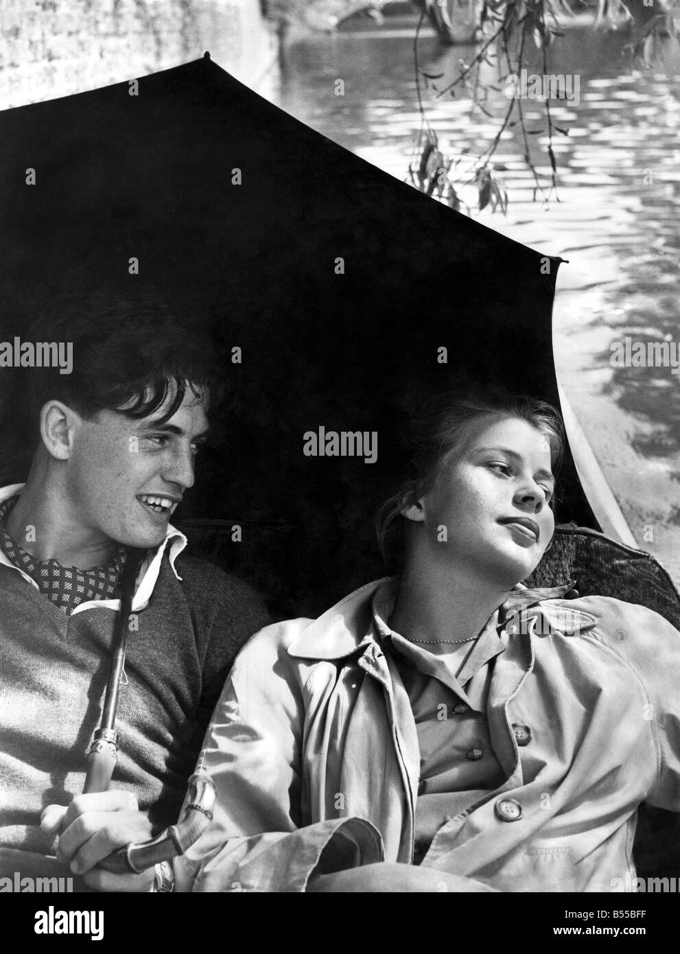 La leçon de langue allemande ou sans larmes : l'endroit est la rivière Cam à Cambridge. Se reposant dans un punt habillé contre les changements météorologiques et prepered avec parasols sont James Innes de premier cycle de St Catherine's College où il lit les langues modernes et Irene Cassel 21 de Göttingen, Basse-Saxe qui est passé un an en Angleterre pour étudier l'anglais. Il s'agit d'Irene's première visite à Cambridge où elle est allée pour la semaine de mai. Que font-ils dans le punt ? Ils échangent des langues. Juin 1954 P012670 Banque D'Images