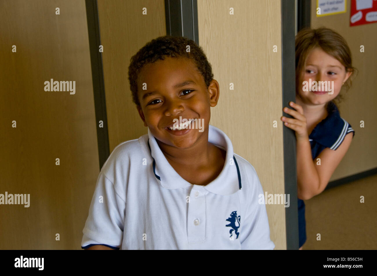 Le garçon sourit à la caméra avec girl peeking schoolfriend autour du coin Banque D'Images