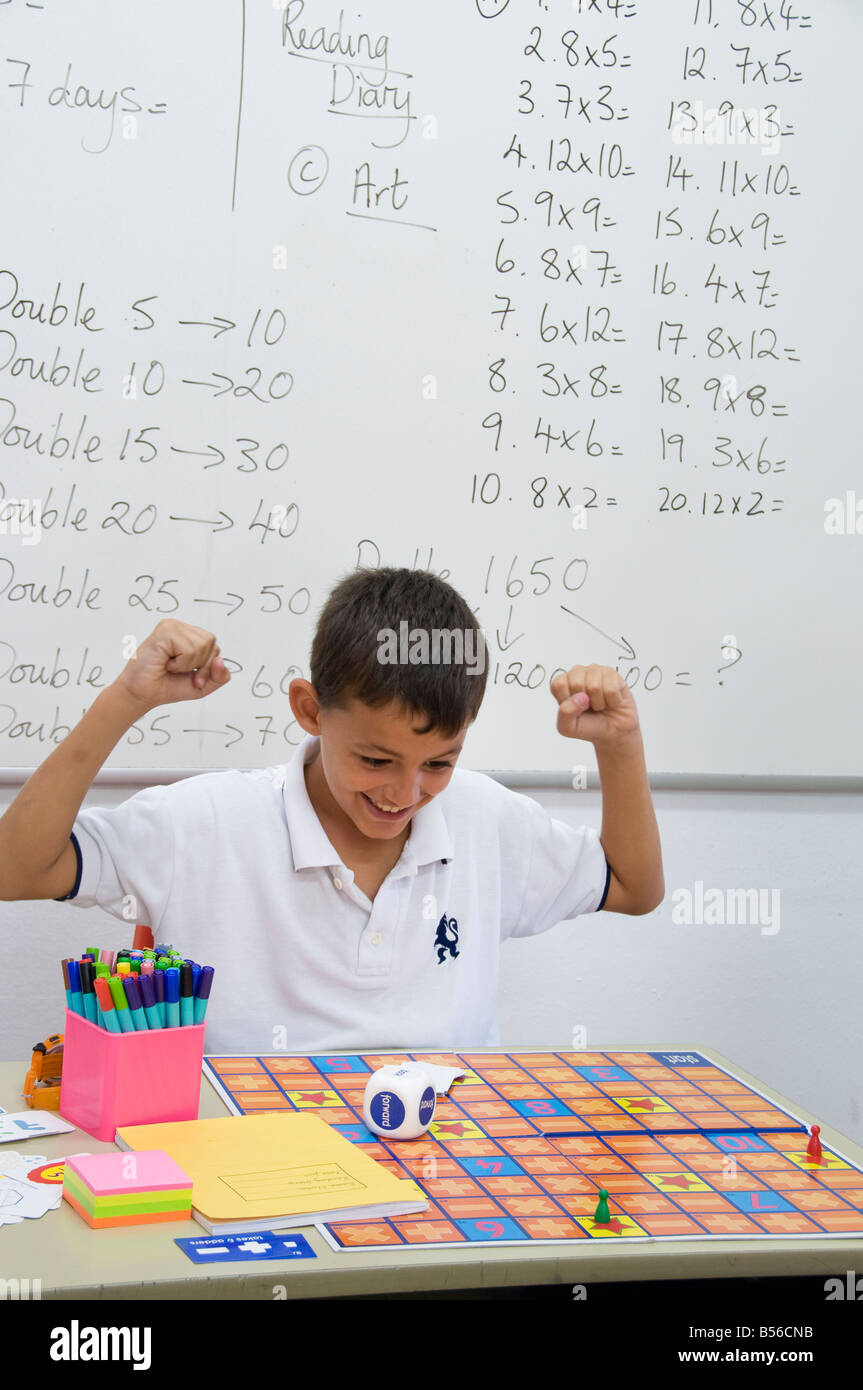 Écolier Junior heureux et excité à son bureau dans la salle de classe de l'école mathématique de jeu jeu ajout Banque D'Images