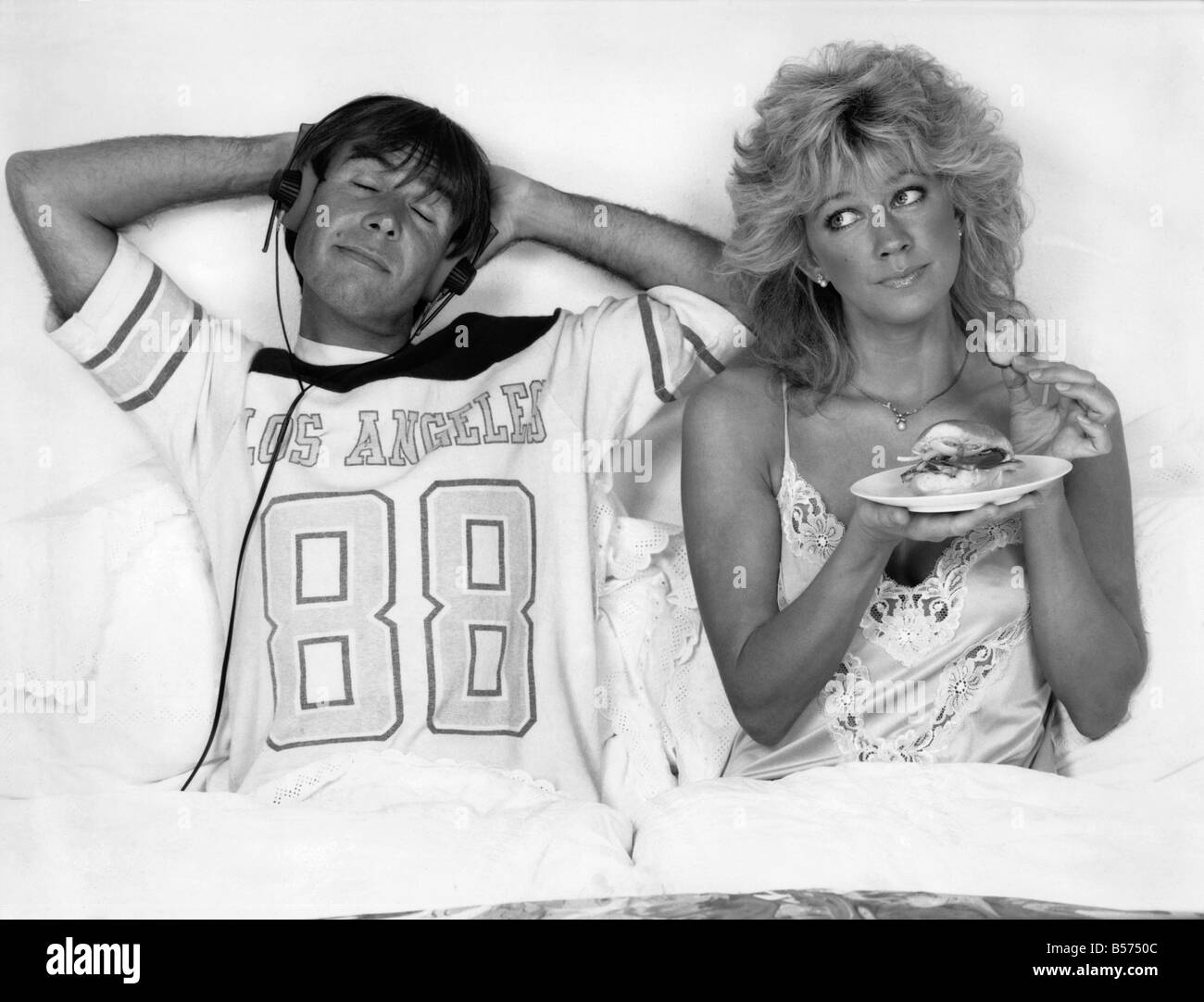 Couple in bed, il écoute de la musique alors que la femme mange. confort. Octobre 1986 P009156 Banque D'Images