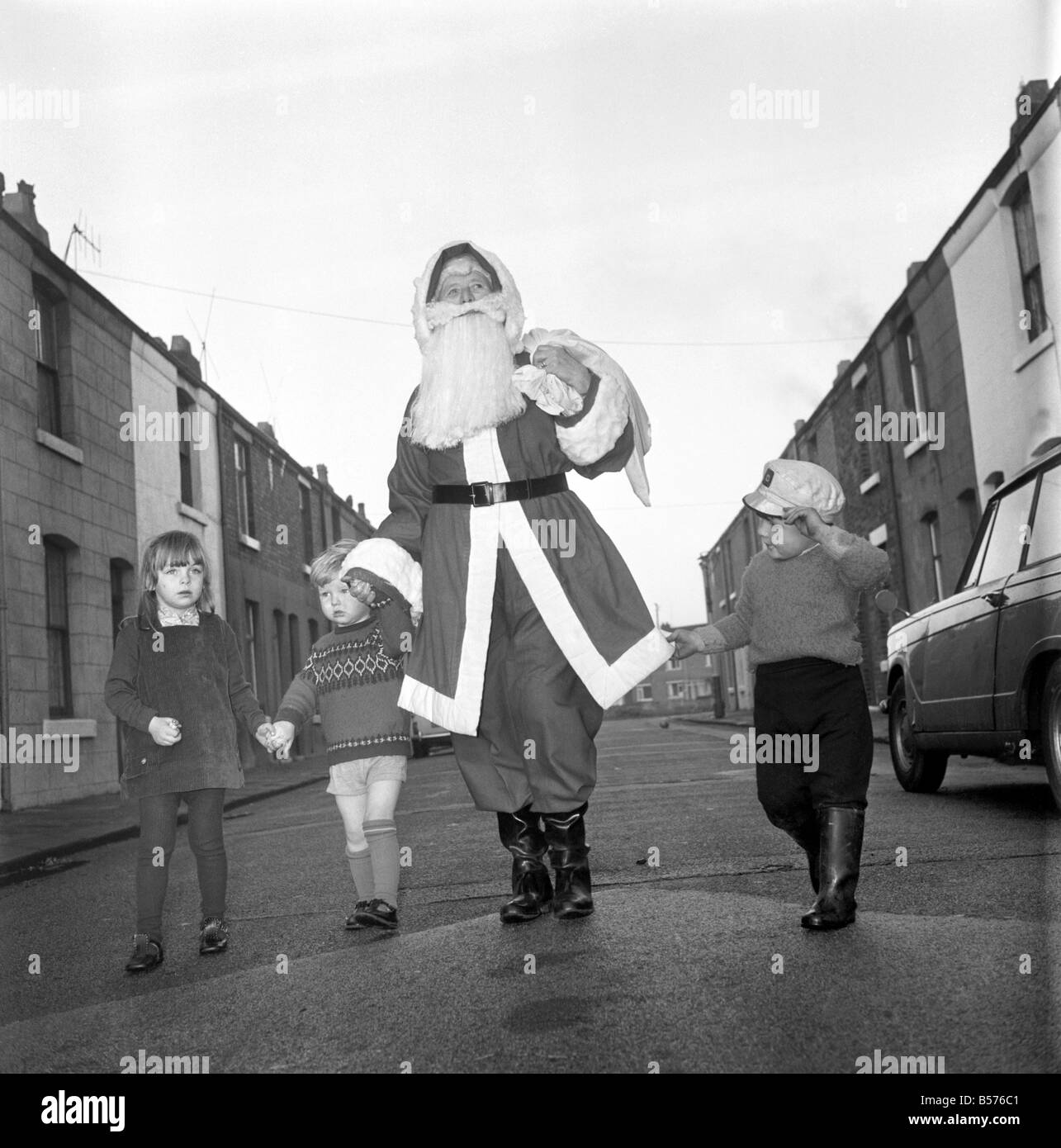 Une vieille femme habillée en Père Noël sur son chemin à un engagement accompagné d'enfants du quartier. Décembre 1969 Banque D'Images