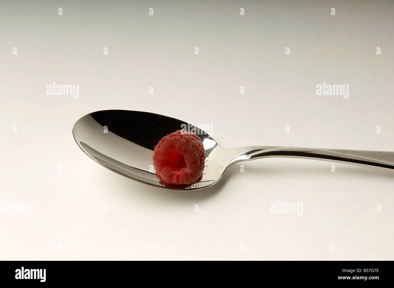 Cuillère en argent avec un fresh red berry framboise sur fond blanc il l'éclairage studio Banque D'Images