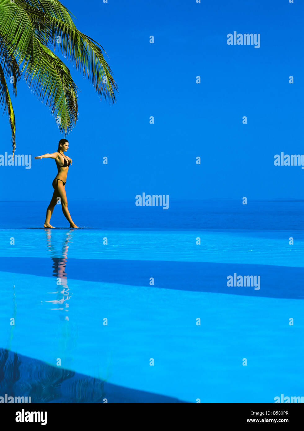 L'équilibrage de femme au bord de la piscine à débordement, Maldives, océan Indien, Asie Banque D'Images