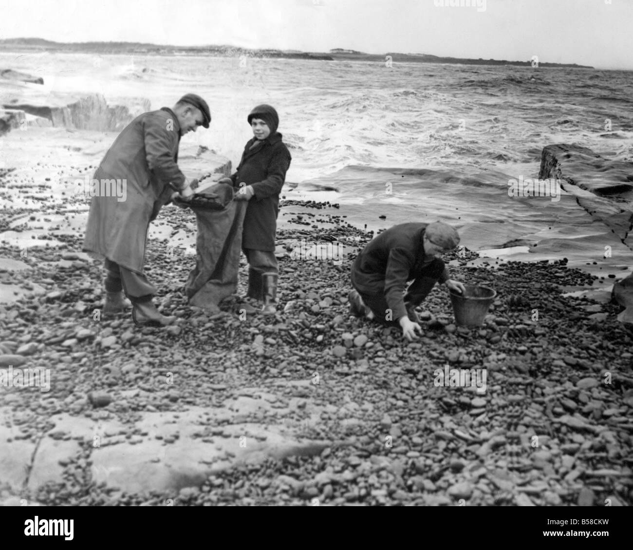 Ignorant la marée montante et le battant du charbon de pulvérisation exploitants travaillent sur les rochers près de la fin de semaine à l'Newbiggin gales et forte mer de le pas quelques jours ont lavé de grandes quantités de charbon sur la mer du Nord à plages de l'Est, certaines personnes font des bénéfices substantiels de la vente du charbon Banque D'Images