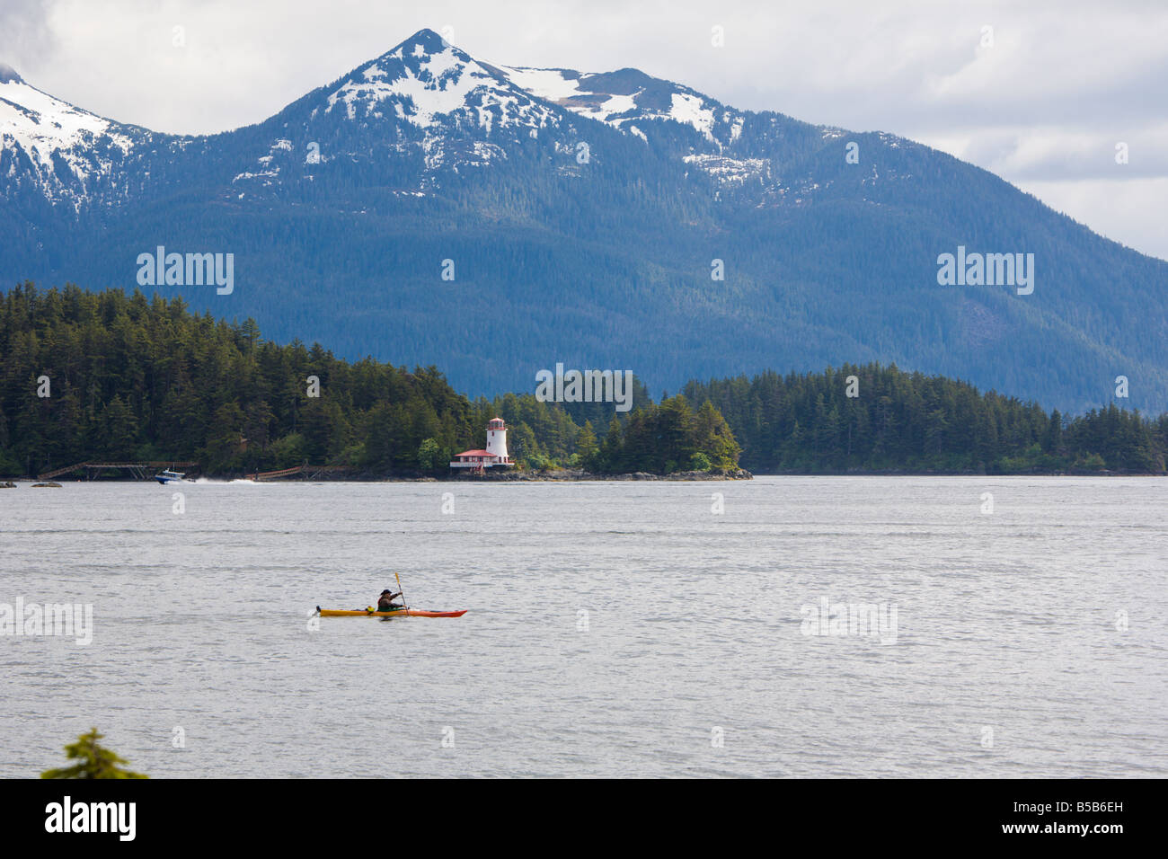 La kayakiste passe devant le phare et les montagnes enneigées en Manche orientale de l'Inside Passage à Sitka, Alaska Banque D'Images