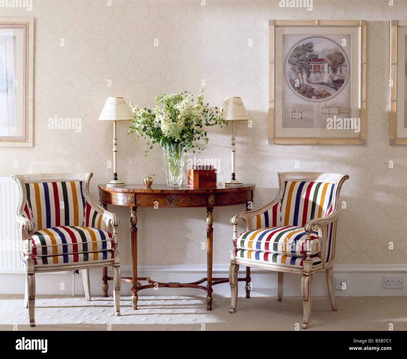 Des fauteuils rembourrés à rayures de couleur de chaque côté de meubles anciens table console en crème traditionnelle hall Banque D'Images
