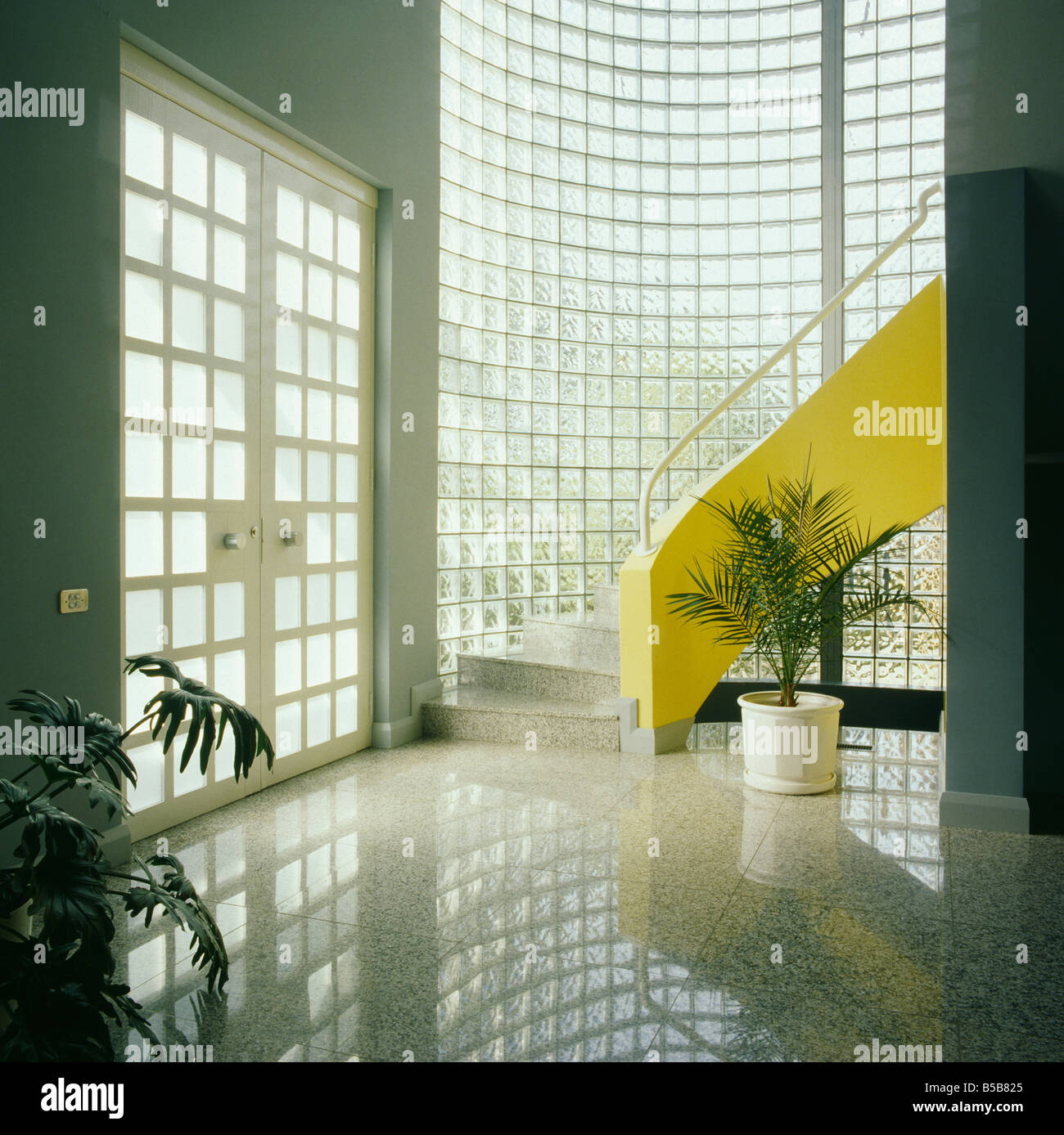Revêtement de sol en granit et de verre mur de brique dans le hall moderne avec escalier jaune et grand double portes Banque D'Images