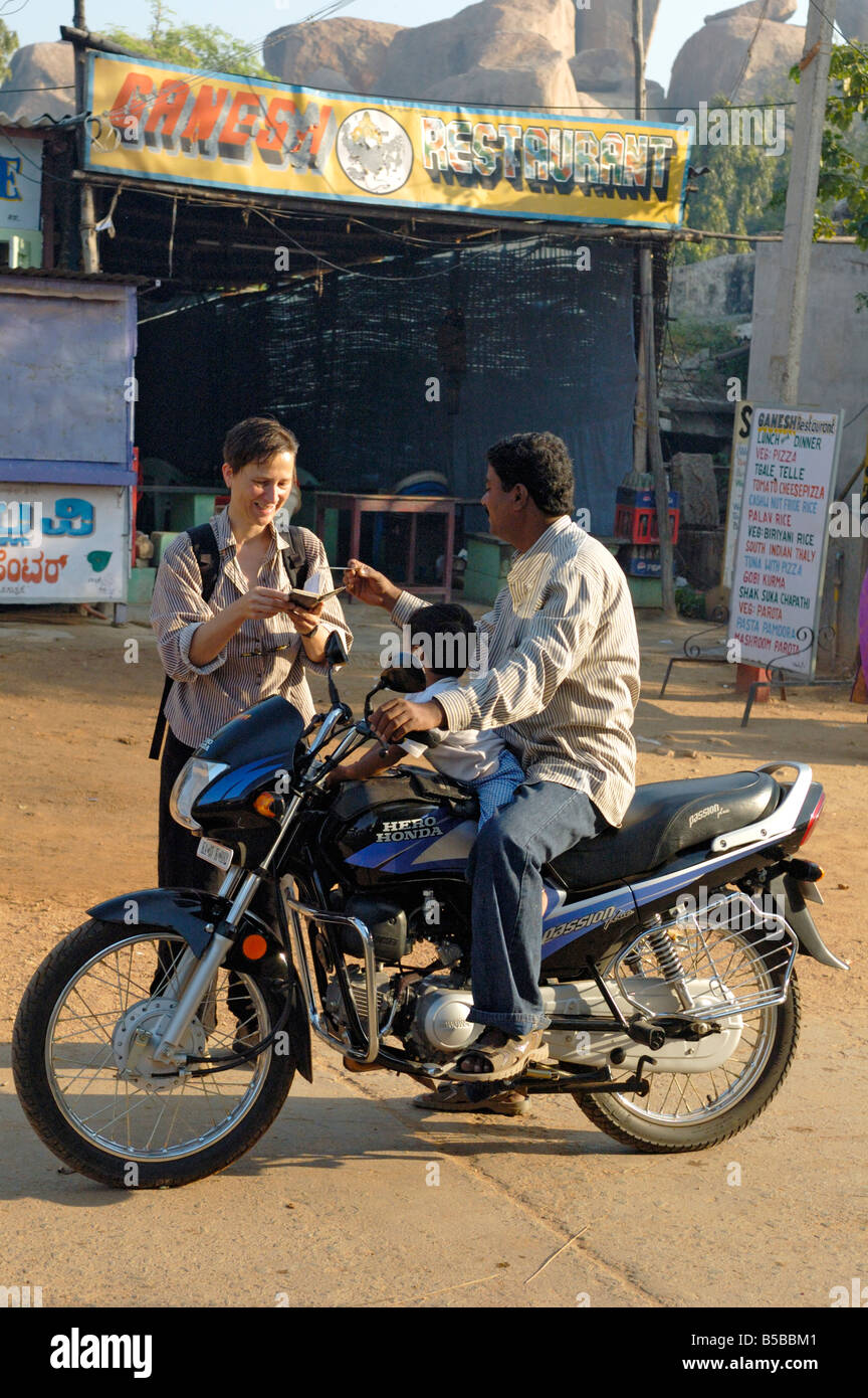 L'allemand woman parler à un guide local officiel assis avec son enfant sur une moto. L'Inde, Karnataka, Hampi Banque D'Images