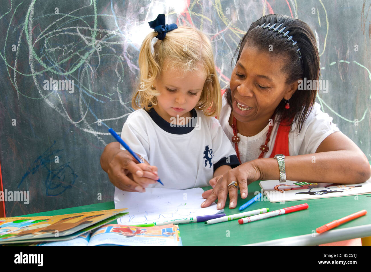 Maternelle femme enseignante entraîneur blonde 3-5 ans bébé fille à dessinez des formes à l'extérieur dans une école de jeux ensoleillée de maternelle Banque D'Images