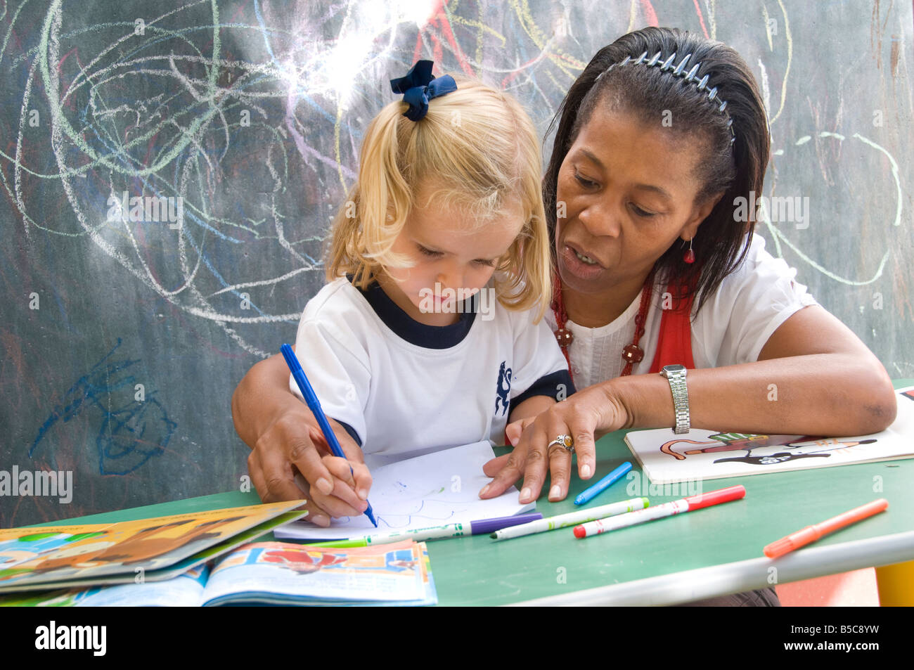 L'encadrement de l'enseignant pour fille bébé dessiner des formes à l'extérieur de la région de sunny ecole maternelle playschool Banque D'Images