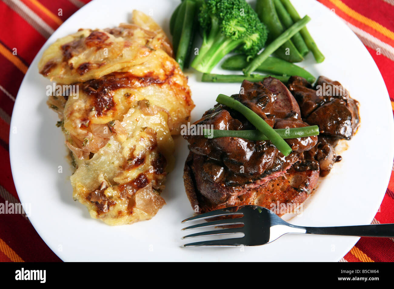 Un repas de boeuf tournedos sur un croûton garni de champignons dans une sauce brune avec des haricots,petits pois et l'oignon et de pommes de terre au gratin Banque D'Images