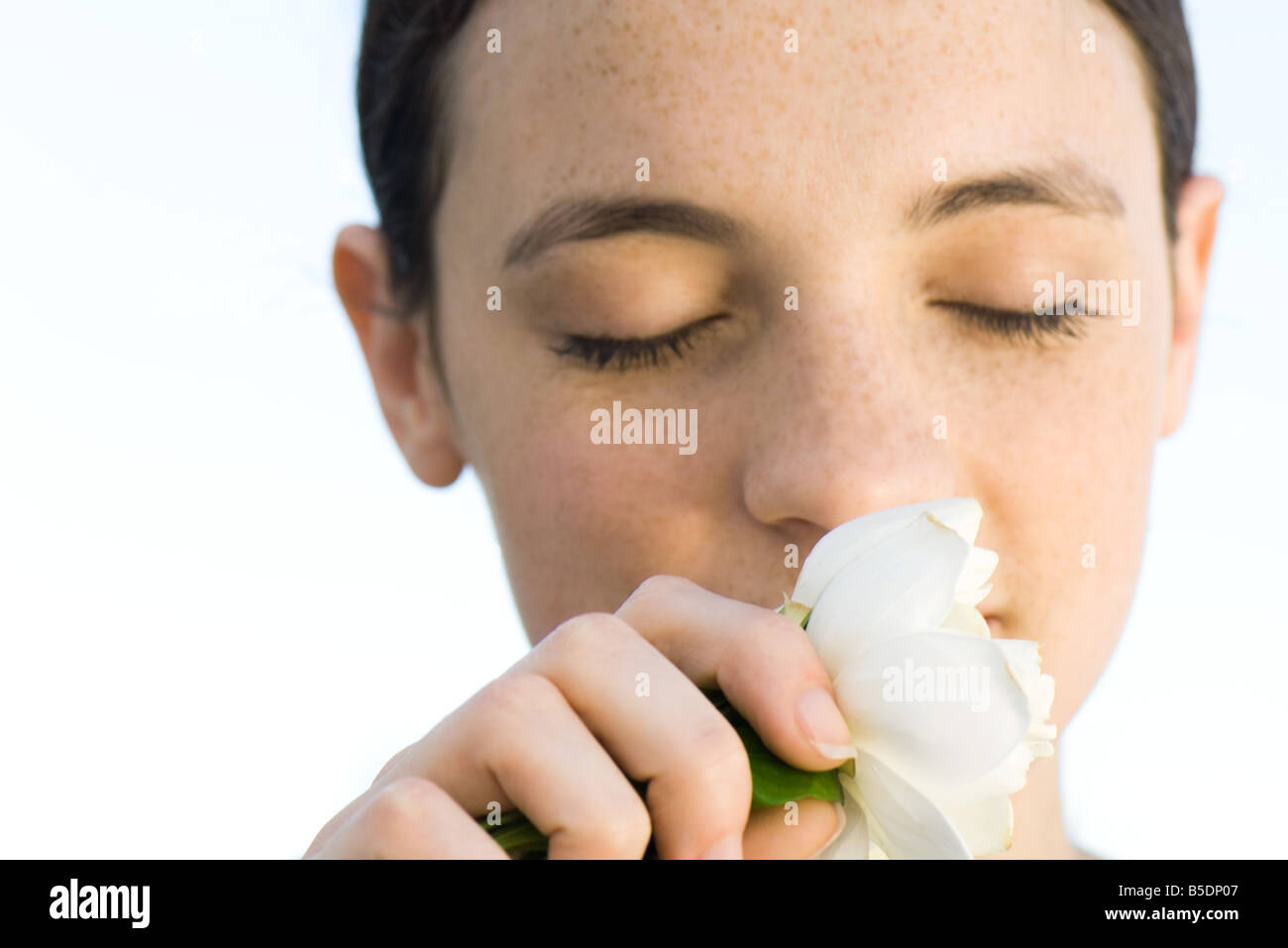 Jeune femme qui sent la fleur rose blanche, les yeux fermés, close-up Banque D'Images