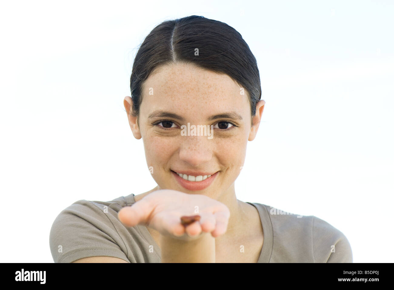 Jeune femme tenant seule graine brune dans la paume de main tendue à l'appareil photo Banque D'Images