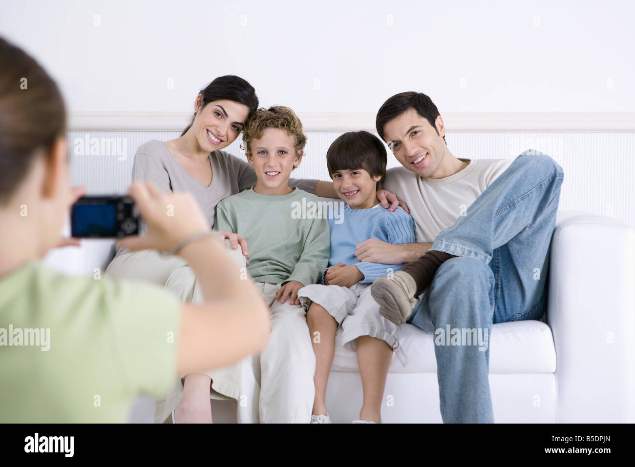 Young Girl taking photo de ses parents et frères assis ensemble sur canapé Banque D'Images