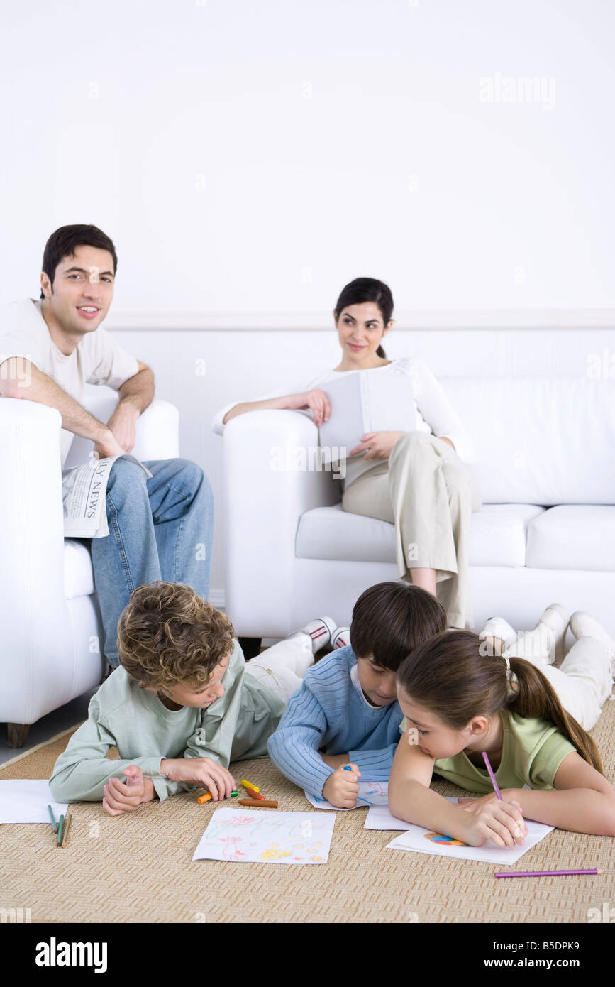 Family relaxing together in living room, les enfants coloration sur marbre, père smiling at camera Banque D'Images