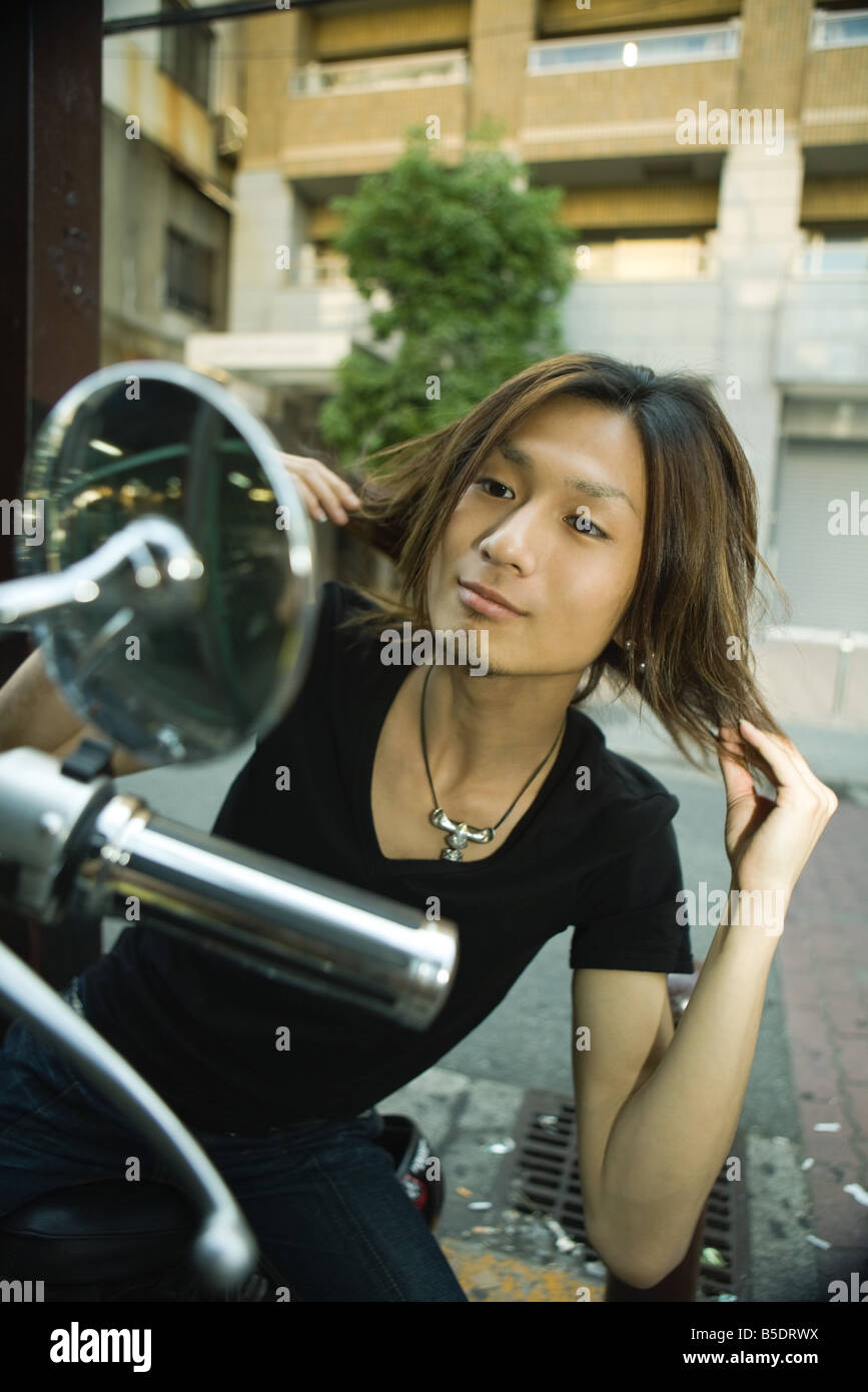 Jeune homme japonais assis sur moto, en cheveux fixation rétroviseur Banque D'Images