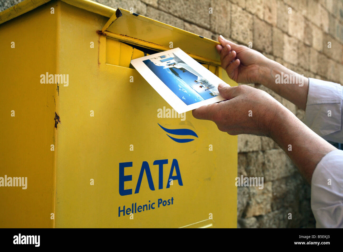 Man throwing une carte postale dans une boîte aux lettres jaune de la poste hellénique, Rhodes, Grèce Banque D'Images