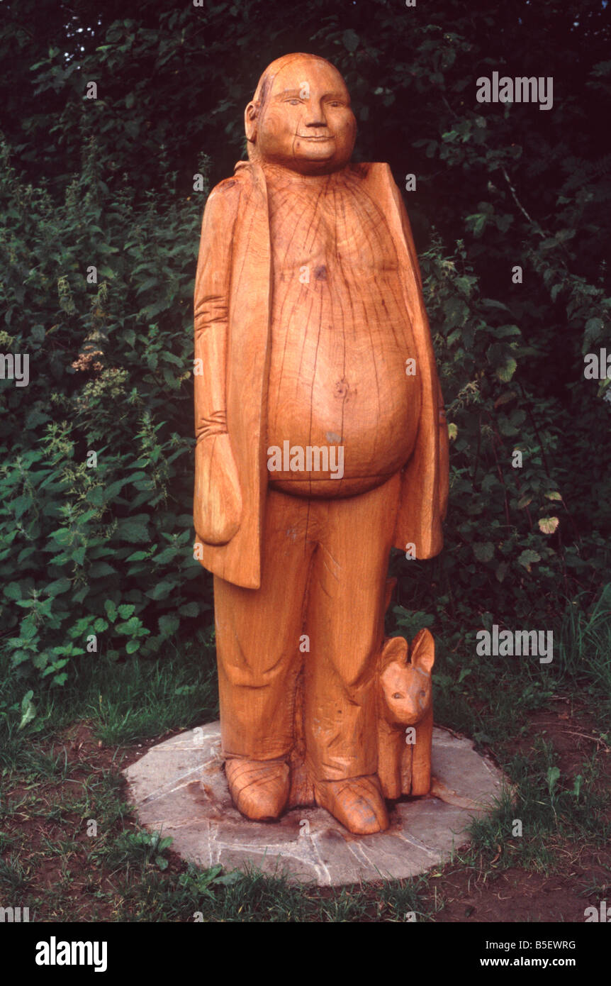 Sculpture en bois d'un grand homme avec le ventre saillant et son chien debout à côté du chemin de halage du canal de Montgomery, Wales Banque D'Images