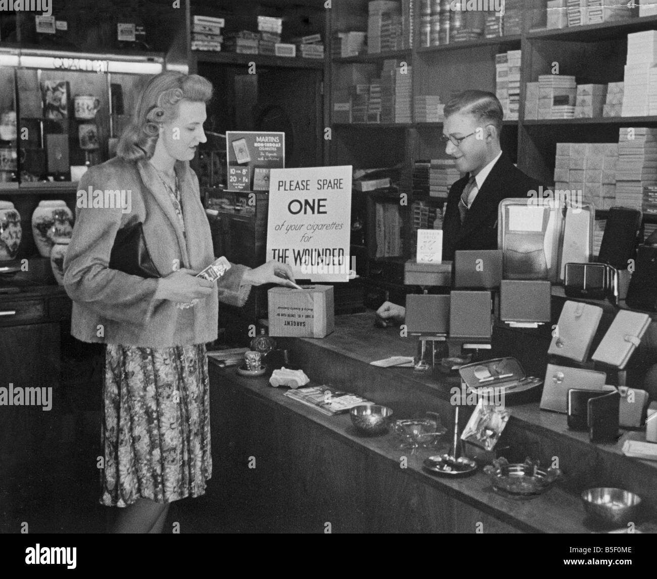 Une femme d'acheter un paquet de cigarettes dans un bureau de tabac shopin Londres, laisse une ampoule de rechange dans une boîte de collecte de cigarettes, qui sera envoyé à un hôpital pour les soldats blessés pendant la Seconde guerre mondiale ;Juin 1940 Banque D'Images