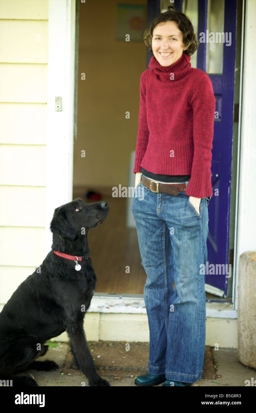 Chiot Golden doodle adoringly regards à son propriétaire dégingandé comme elle se tient et rit avec les mains dans les poches dans l'entrée de sa maison Banque D'Images