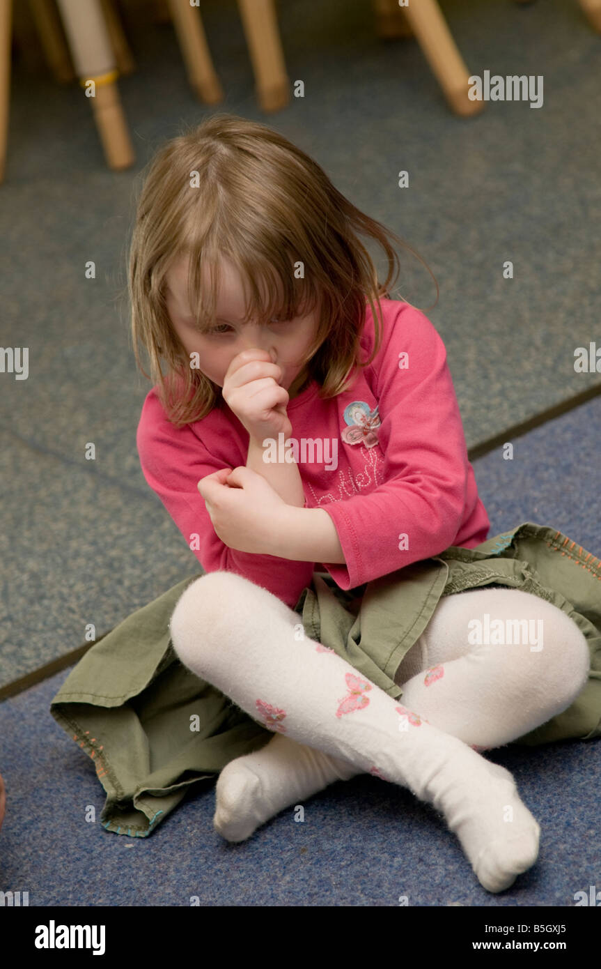 Jeune enfant en crèche garderie fille triste et solitaire à sucer son pouce assis sur le plancher crosslegged Banque D'Images
