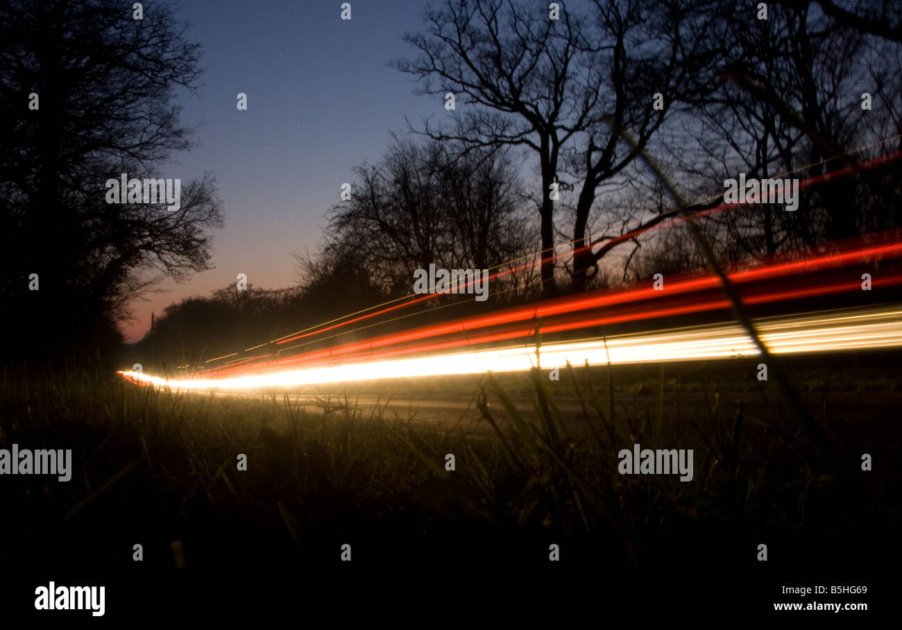 Sentier lumineux des voitures qui traversent la forêt d'Epping au crépuscule. Banque D'Images