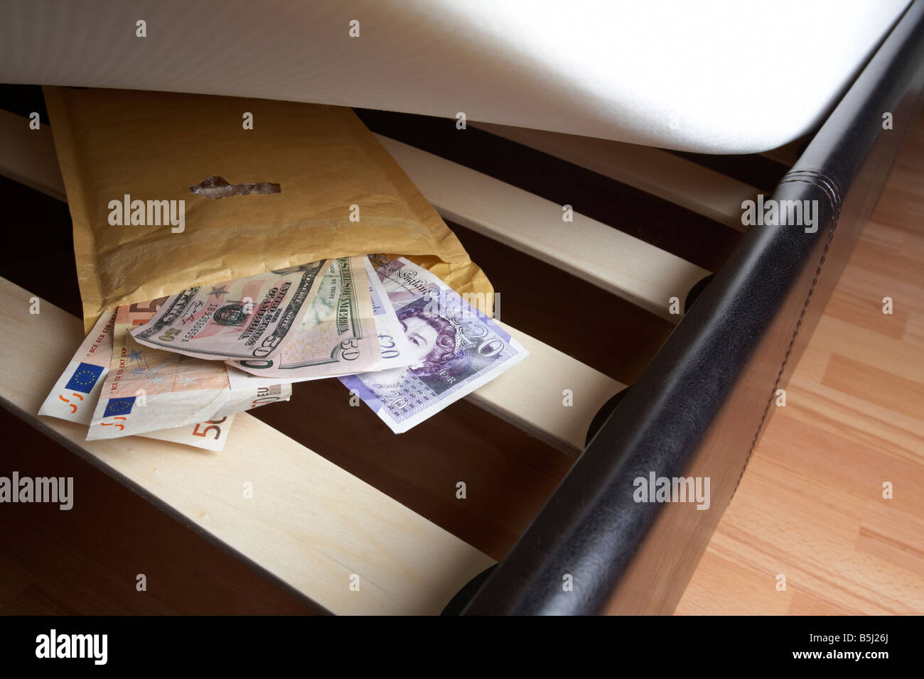 Wad mixte de service de livres sterling Euros et dollars en espèces dans une enveloppe sous le matelas en peluche d'un lit Banque D'Images