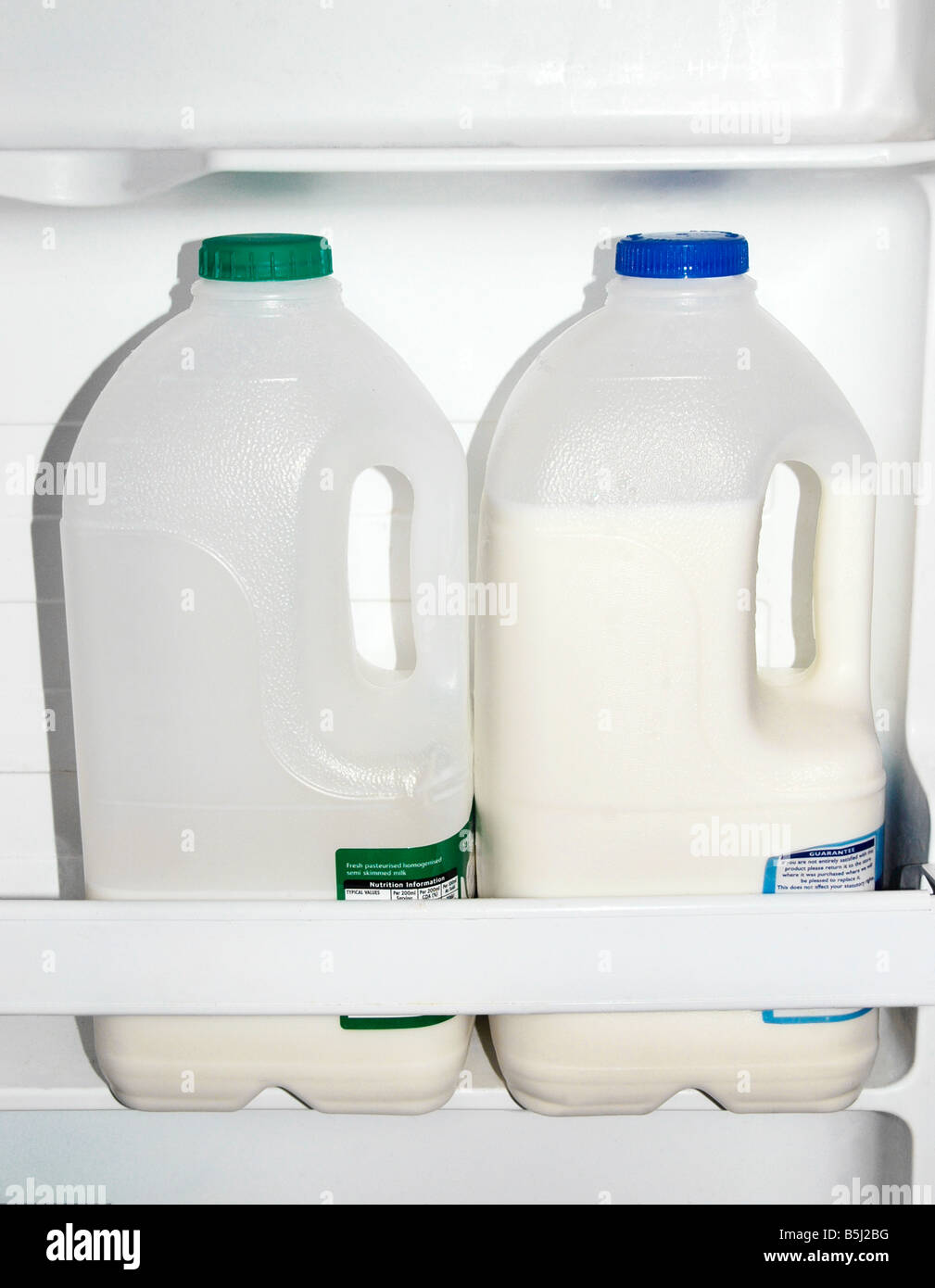 Les bouteilles en plastique de lait écrémé et la crème semi plein de lait dans la porte du compartiment d'un réfrigérateur. Banque D'Images